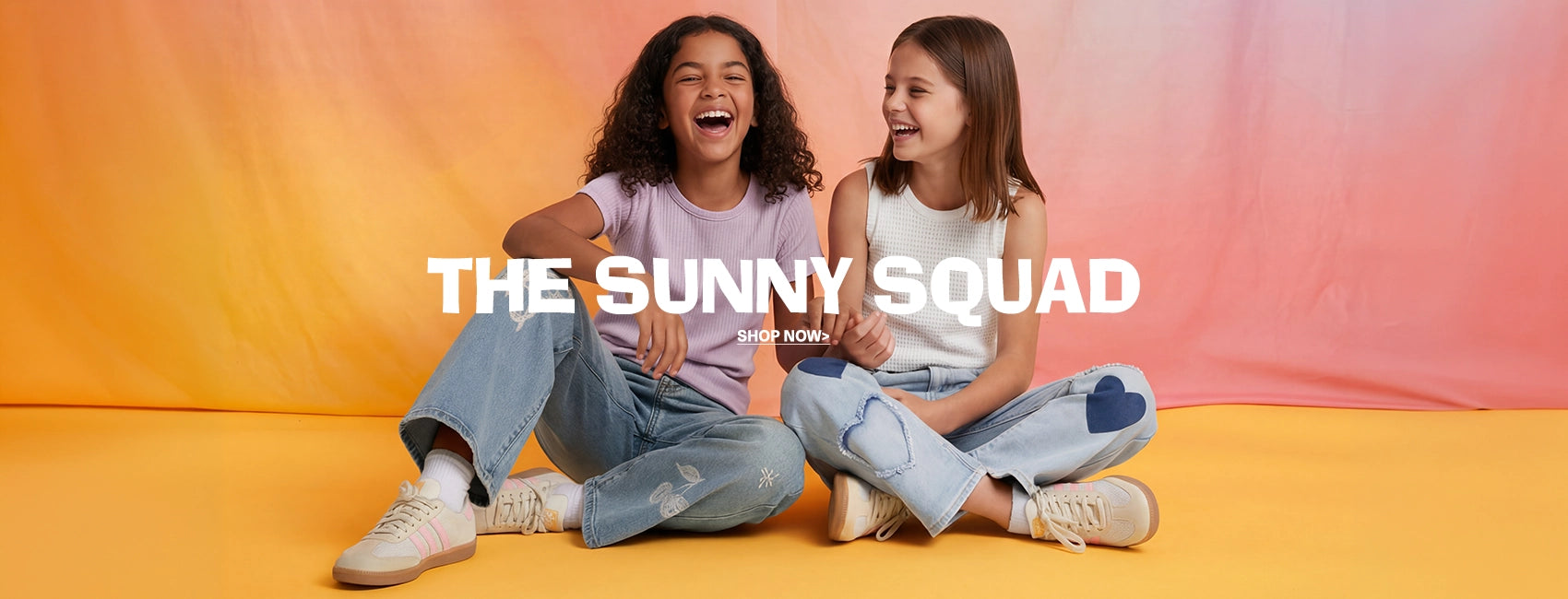 Two young women sitting on a yellow floor with an orange gradient background, smiling and posing for a promotional image with 'The Sunny Squad' text.