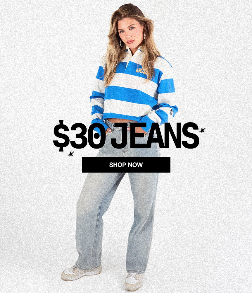 A woman modeling light-wash blue jeans with a blue and white striped long-sleeve top, standing against a light textured background with a '$30 JEANS' and 'SHOP NOW' promotional overlay.